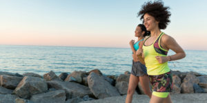 Women_running_near_ocean_rocks_with sunset