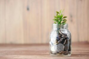 Glass jar sitting on table with coins in the jar and a plant sitting on top.