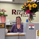 Picture of female teller with a vase of flowers on each side of counter.