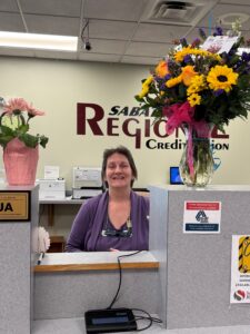 Picture of female teller with a vase of flowers on each side of counter.